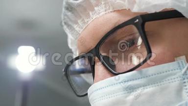 戴着手术面罩的眼镜的外科医生低头<strong>看病</strong>人，然后站在监视器或助手旁边。 行动